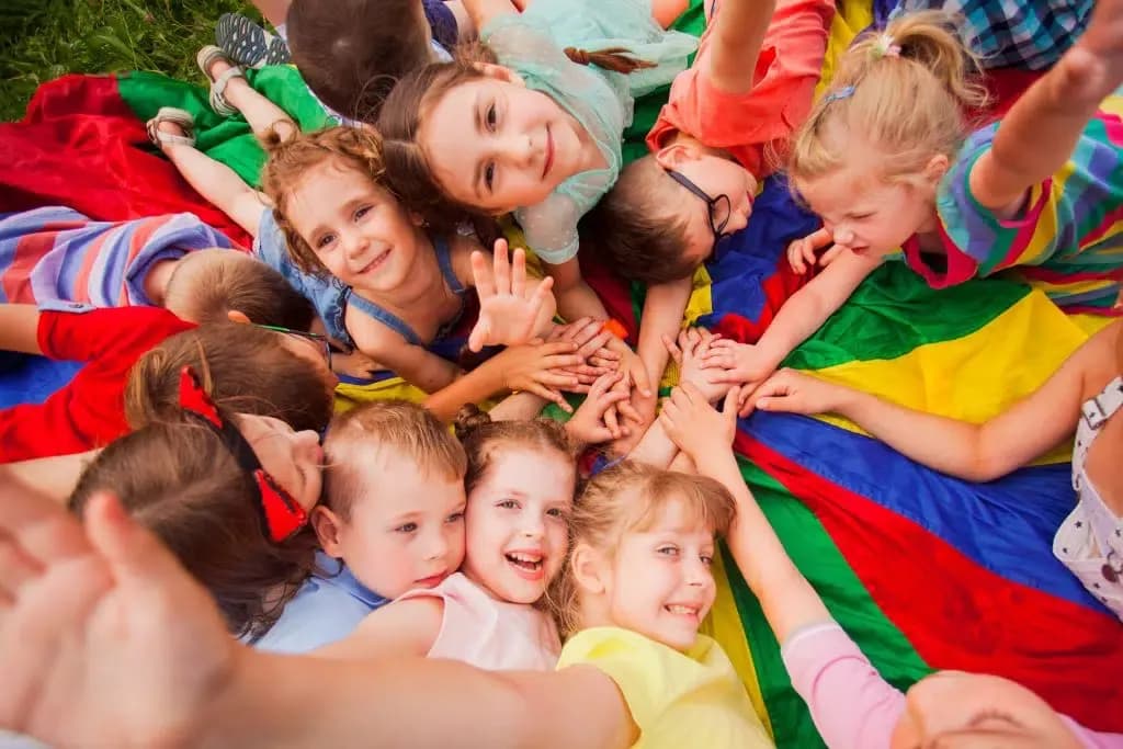 Children play outside on a rainbow parachute.