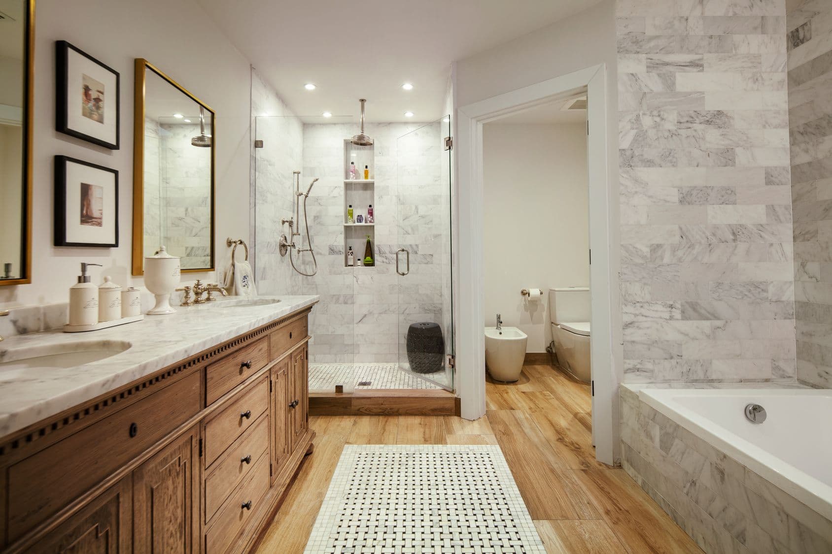 Luxury master bathroom with marble-tiled walk-in shower, wooden vanity, large mirror, soaking tub, and hardwood floors