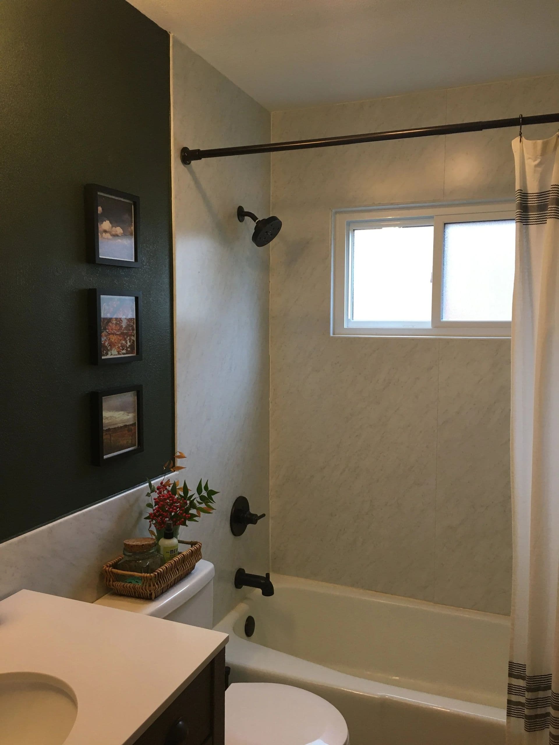 A dark-colored bathroom with light gray marbled walls, combination shower tub, and matte black fixtures.