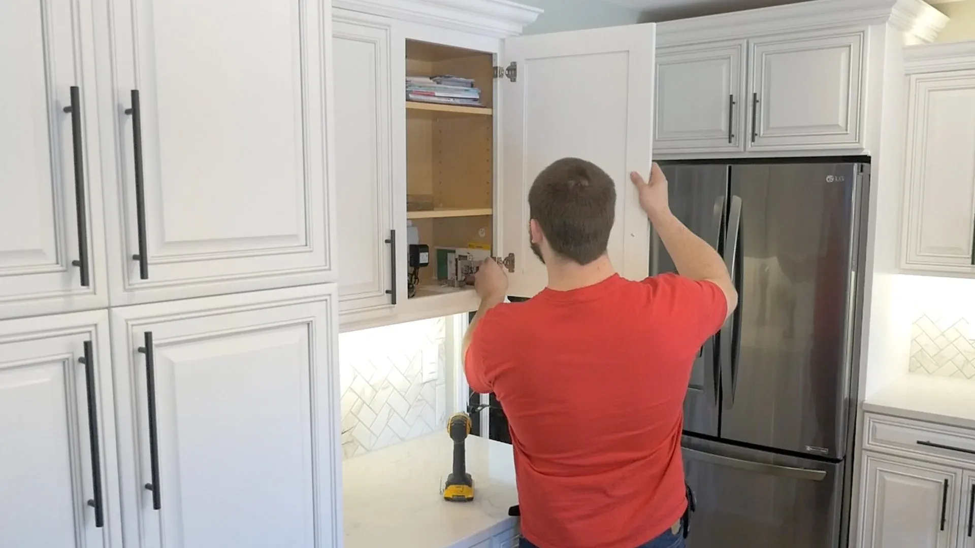 A worker installs a newly-refaced white kitchen cabinet door.