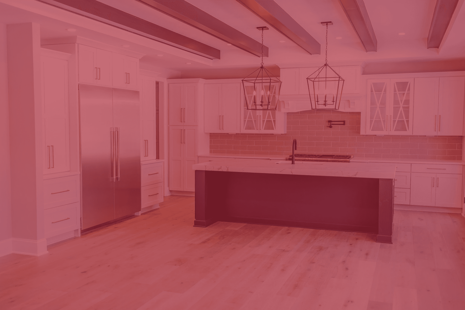 A kitchen with white cabinets and gold fixtures, large central island with dark navy blue base, gray tile backsplash, exposed metallic ceiling beams, and stainless steel appliances.