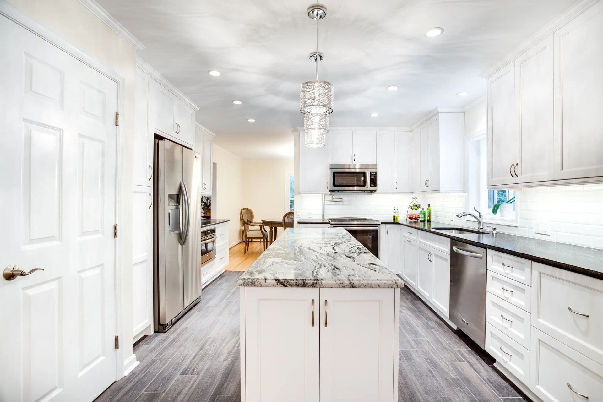 A kitchen with white cabinets, gray flooring, central island with gray marbled countertop, and stainless steel appliances.
