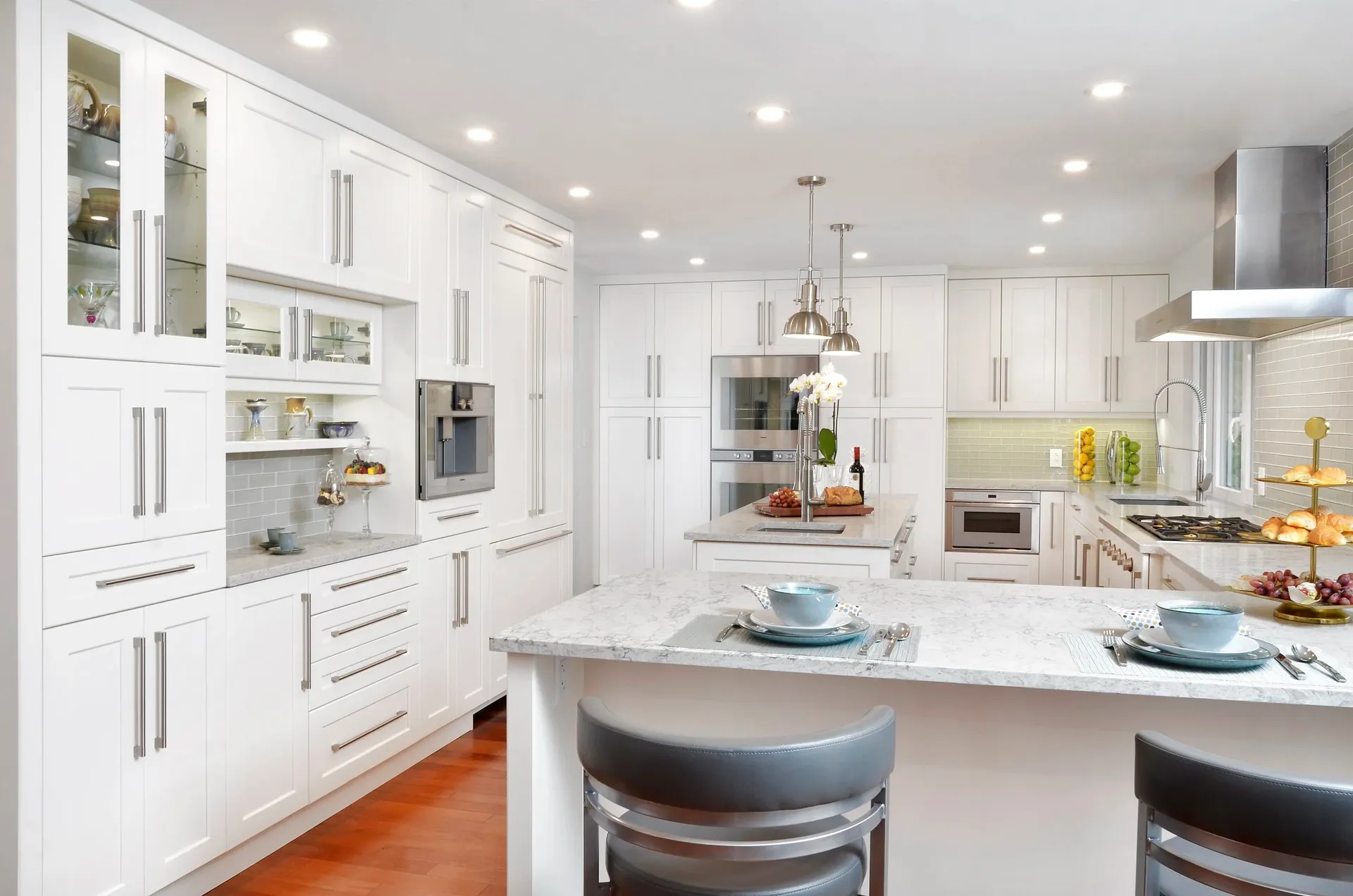 A newly-remodeled kitchen with white cabinets, light-colored marbled countertops, central island, and breakfast bar with stool seating.