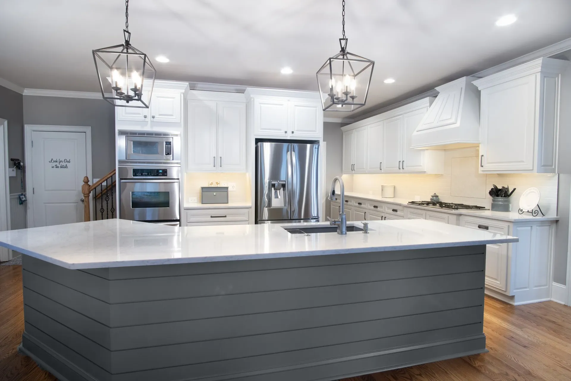 A gray kitchen with white cabinets, large central island, white countertops, and stainless steel appliances.