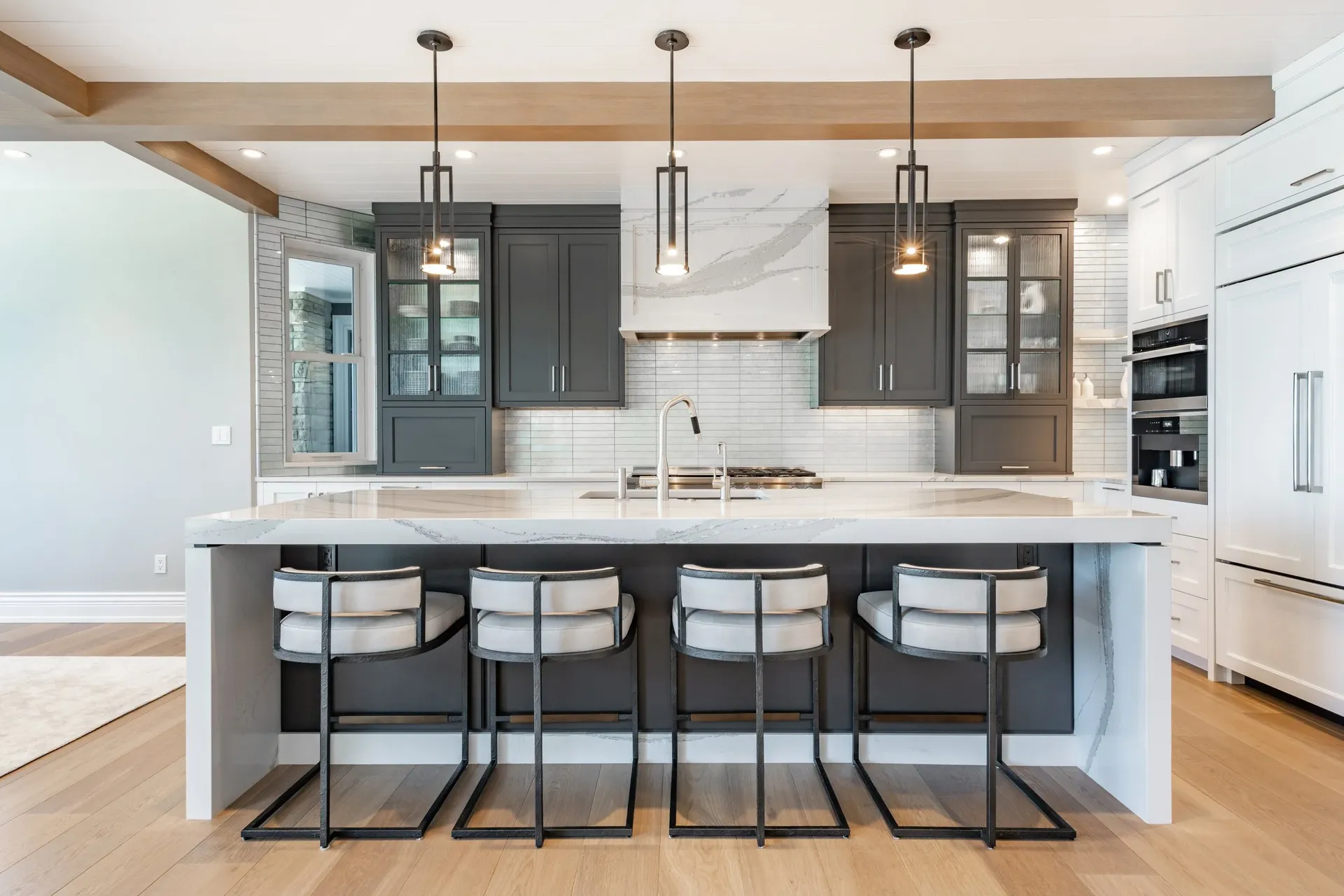 A white kitchen with dark gray cabinets and center island with white marble top and four white bar stools.