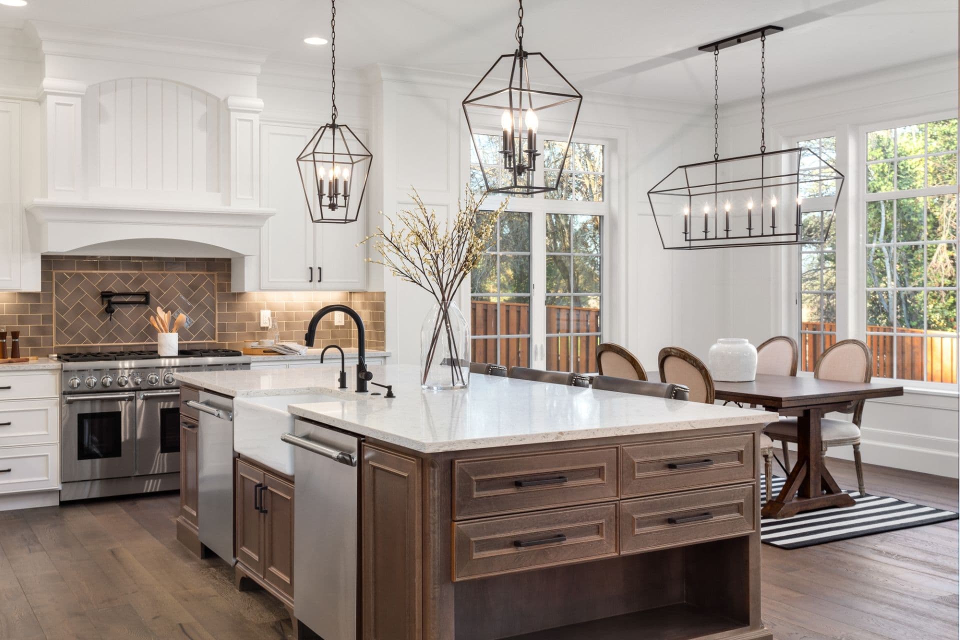 A kitchen with white cabinets, stainless steel appliances, center island with brown cabinets, white countertops, and black fixtures.