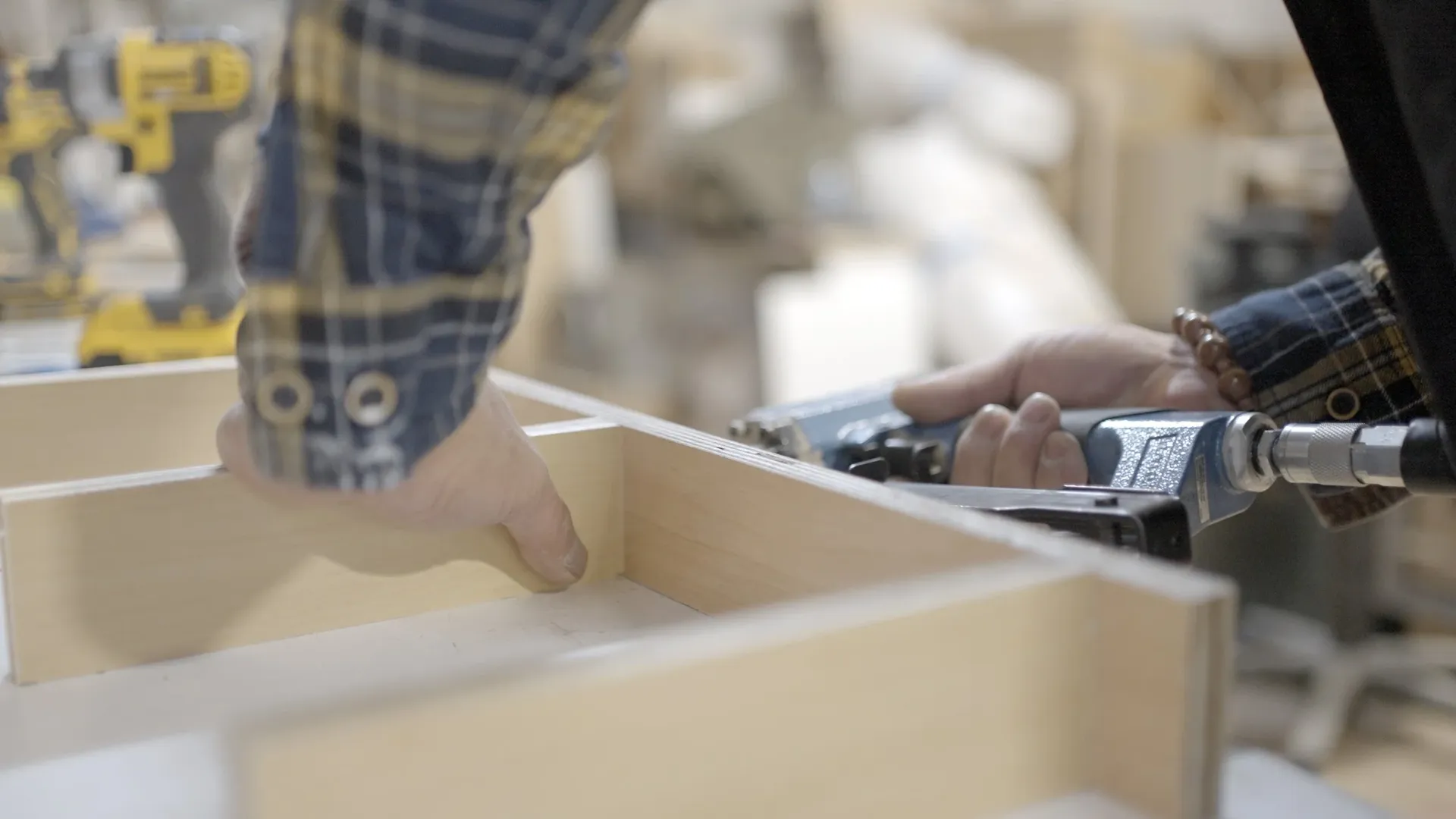 A close-up of a worker using a nail gun on kitchen cabinets.
